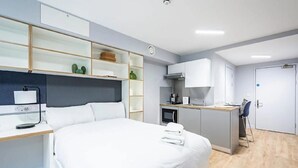Una habitación de hotel moderna con una cama grande, un escritorio con una computadora, una kitchenette y un baño.