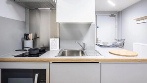 Cocina moderna con un lavamanos de acero inoxidable, estufa y campana extractora. Cuenta con encimera de madera y un mueble blanco.