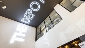 Un interior moderno con un llamativo letrero de 'THE DEPOT' en el techo, ventanas amplias y un diseño limpio y minimalista.