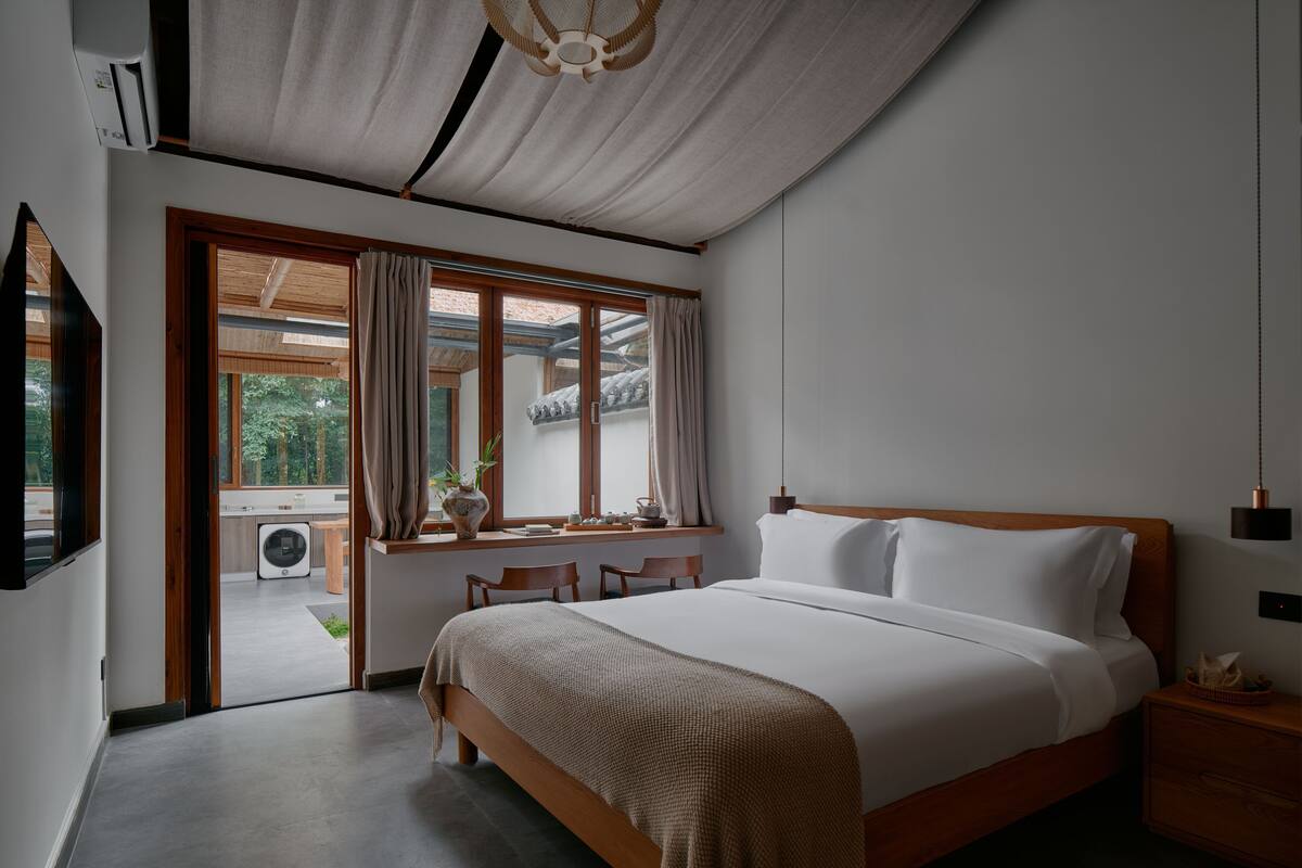 A modern bedroom with a large bed, wooden headboard, and a view of a traditional building through a window.