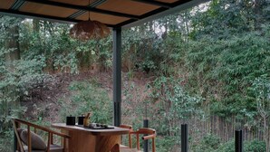 A dining area with a wooden table and chairs, surrounded by a glass wall with a view of a lush garden. - Jishang Qingcheng Mountain Villa (Chengdu)