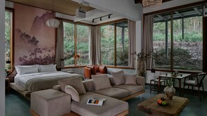 A modern bedroom with a large bed, a sofa, a dining table, and a view of the forest through large windows. - Jishang Qingcheng Mountain Villa (Chengdu)