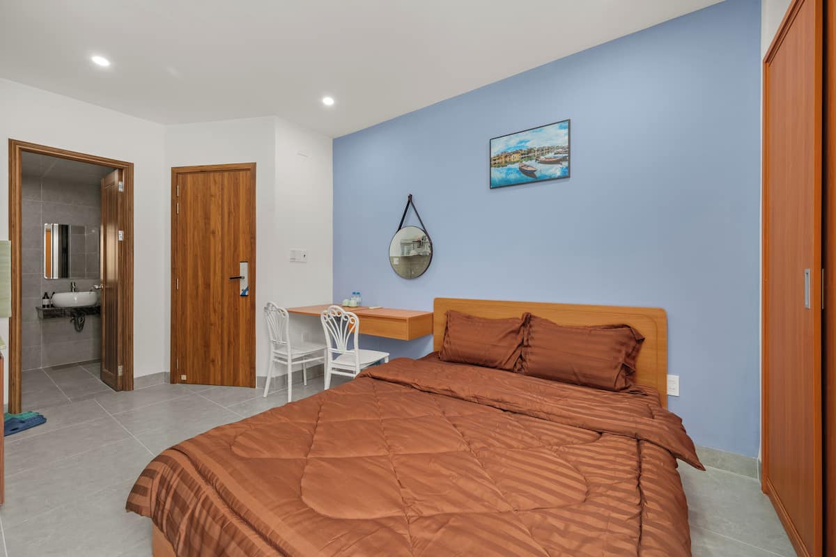 A bedroom with a bed, a desk, a chair, a mirror, and a painting on the wall.