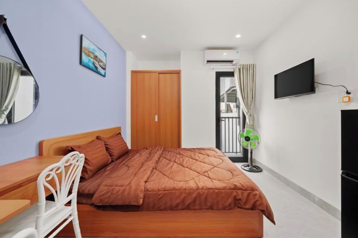A bedroom with a bed, a desk, a chair, a TV, and a window with curtains.