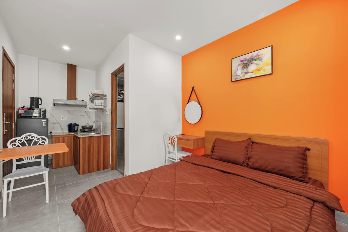 A bedroom with a large bed, a wooden headboard, and a bright orange accent wall.