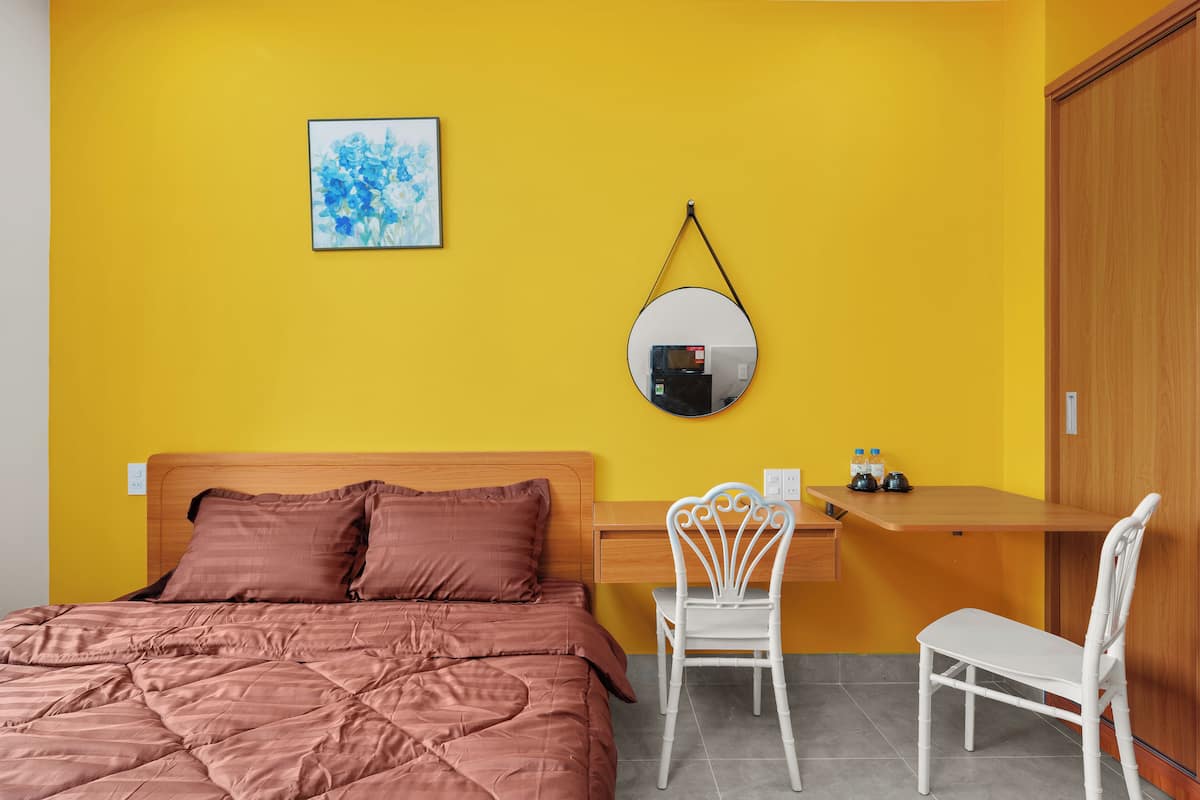 A room with a bed, a desk, two chairs, a mirror, and a painting on the wall.