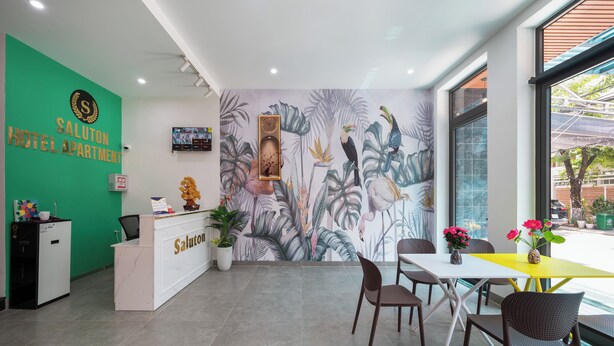 A hotel reception area with a green wall, a reception desk, a clock, and a tropical mural. - Saluton House (Da Nang)