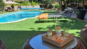 A poolside area with lounge chairs, a table with drinks, and a well-maintained lawn. - Le MAS CLEMENTINE (Puisserguier)