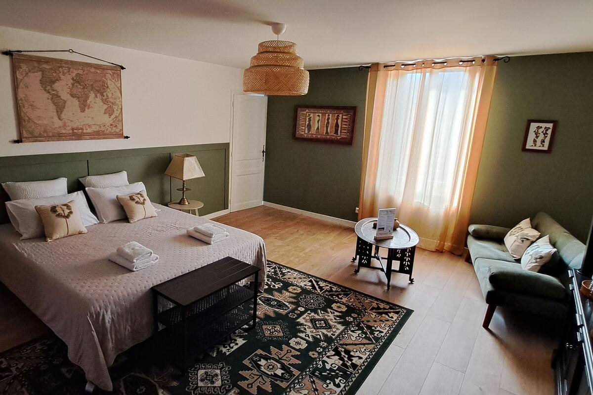 A bedroom with a bed, bedside tables, a sofa, a small round table, a hanging lamp, and a world map on the wall.