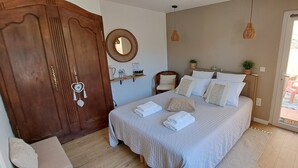 A bedroom with a bed, a wooden wardrobe, a mirror, a shelf with toiletries, and a view of the outside. - Le MAS CLEMENTINE (Puisserguier)