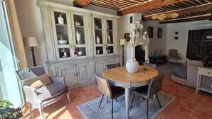 A dining area with a round wooden table, chairs, a cabinet with glass doors, and a fireplace. - Le MAS CLEMENTINE (Puisserguier)