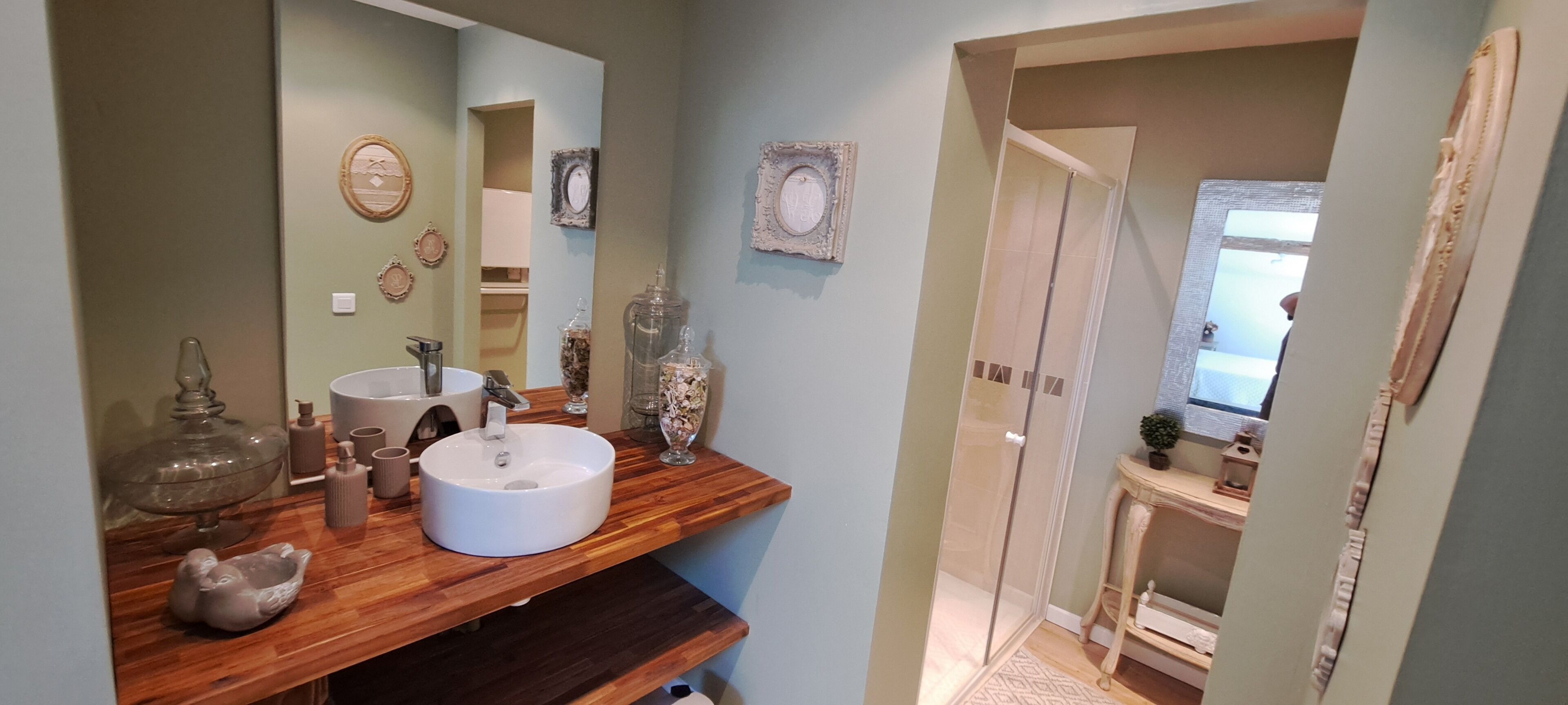 Ein Badezimmer mit einem Holzwaschtisch, einer weißen Spüle und Dekoration. Über der Spüle befindet sich ein Spiegel und eine Tür, die zu einem anderen Raum führt.