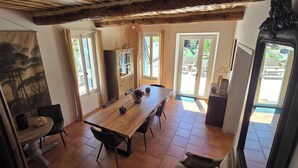 A dining area with a wooden table, chairs, and a view of the garden through glass doors. - Le MAS CLEMENTINE (Puisserguier)