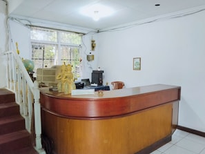 Un mostrador de recepción con detalles de madera, un globo terráqueo y una estatua. A la izquierda, una escalera con barandillas blancas.