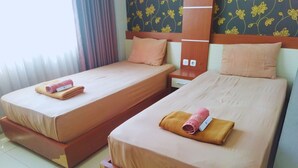 Two single beds with matching brown bedding and pillows, a wooden nightstand with a drawer, and a patterned wall behind the beds. - Hotel Karunia PKPRI (Purwodadi)