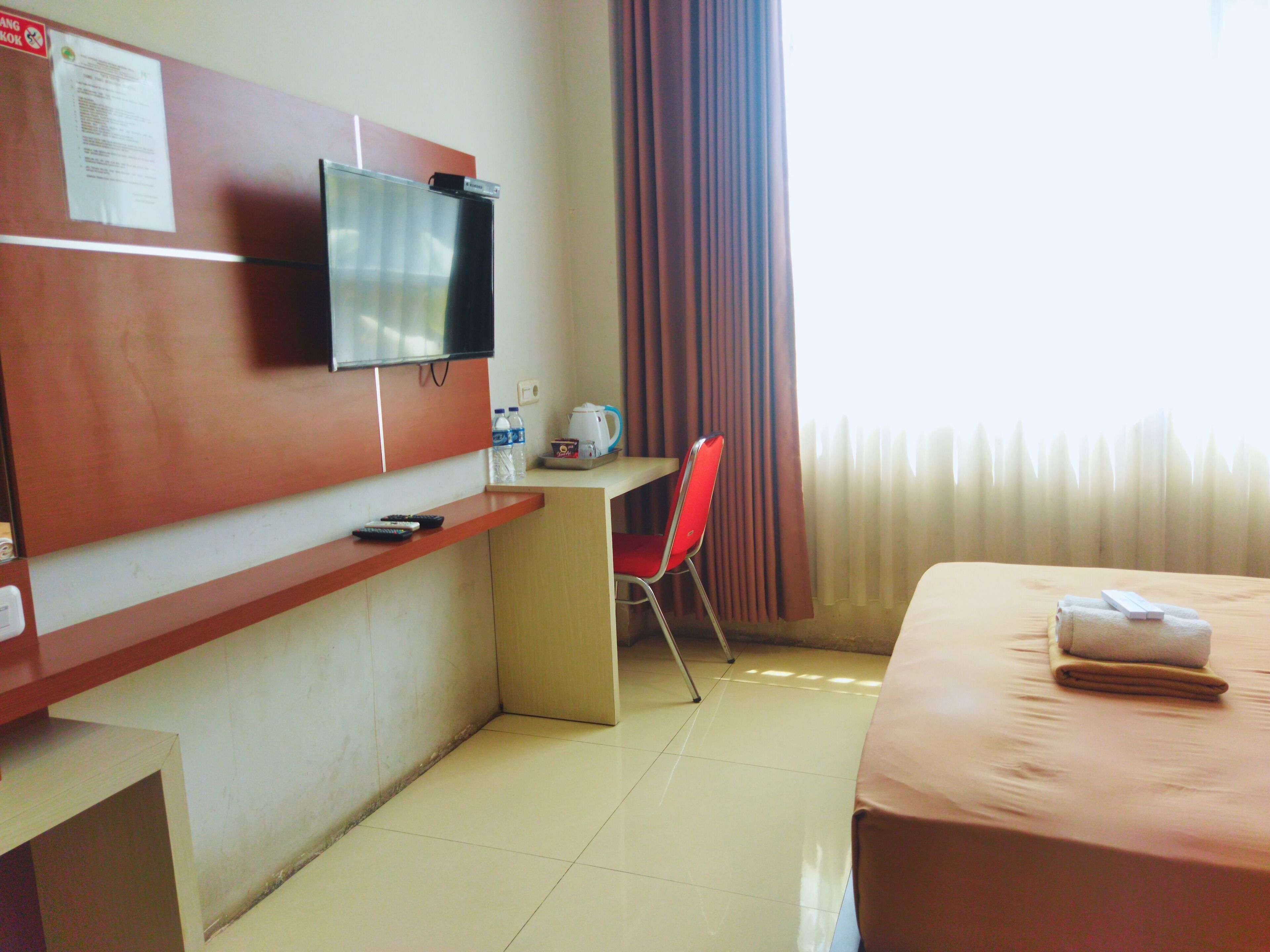 Une chambre d’hôtel équipée d’un lit, d’un bureau, d’une chaise, d’une télévision et d’une fenêtre avec des rideaux.