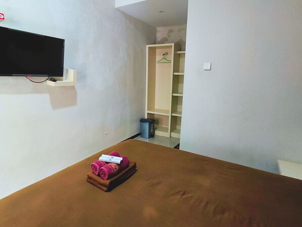 A room with a bed, a TV mounted on the wall, a small trash bin, and a closet with a hanger. - Hotel Karunia PKPRI (Purwodadi)