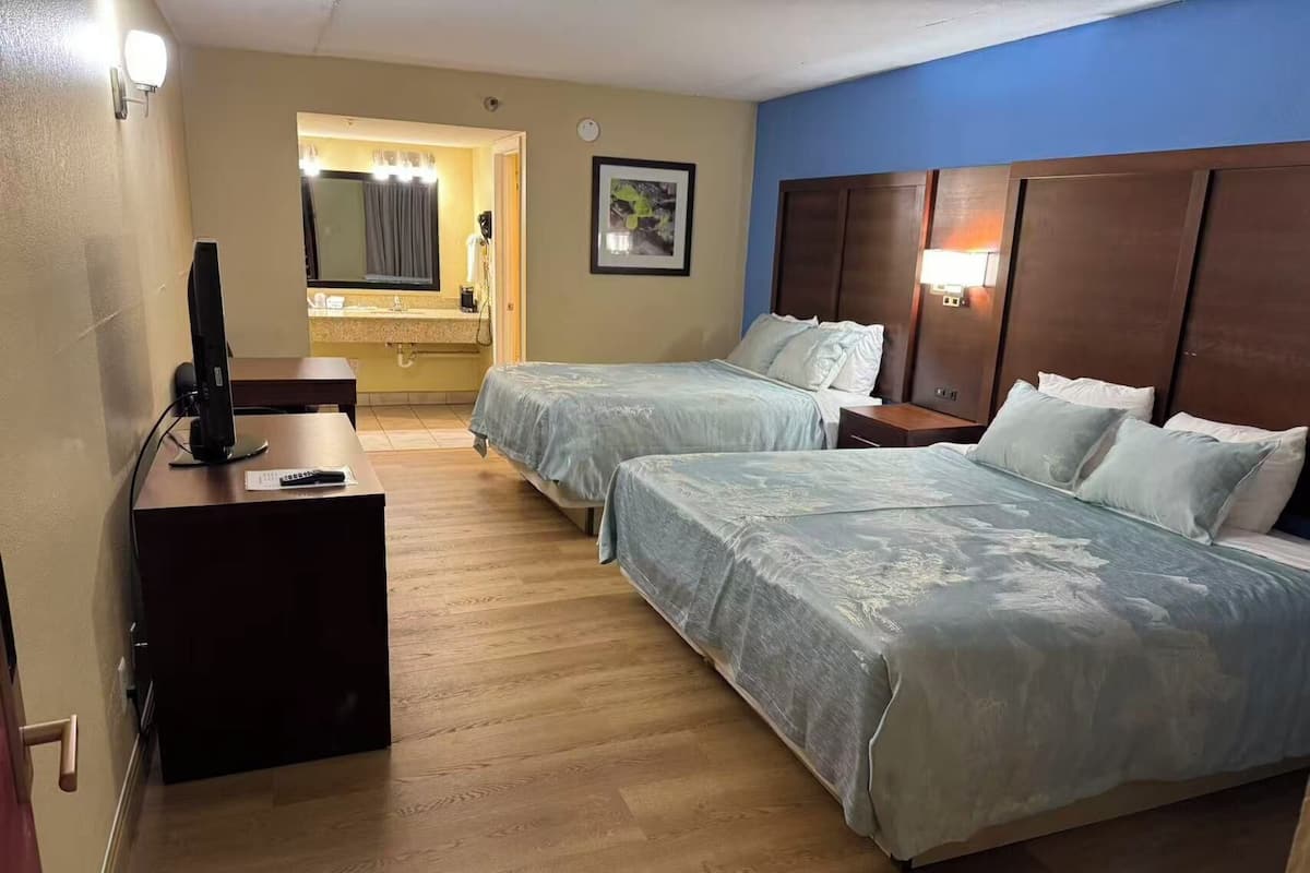 A hotel room with two beds, a desk with a computer, a mirror, and a bathroom visible through an open door.