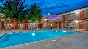 A hotel with a swimming pool, multiple rooms with balconies, and a sunset sky.