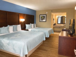 Habitación de hotel con dos camas, un escritorio, un espejo y un baño visible a través de una puerta abierta.