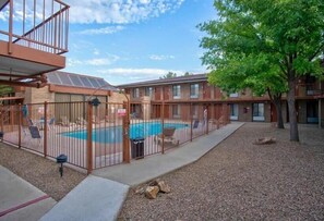 Une piscine entourée d’une clôture, avec des chaises longues et un bâtiment doté de nombreuses fenêtres et de balcons.