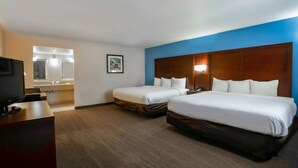A hotel room with two beds, a TV, a desk, and a bathroom visible through an open door.