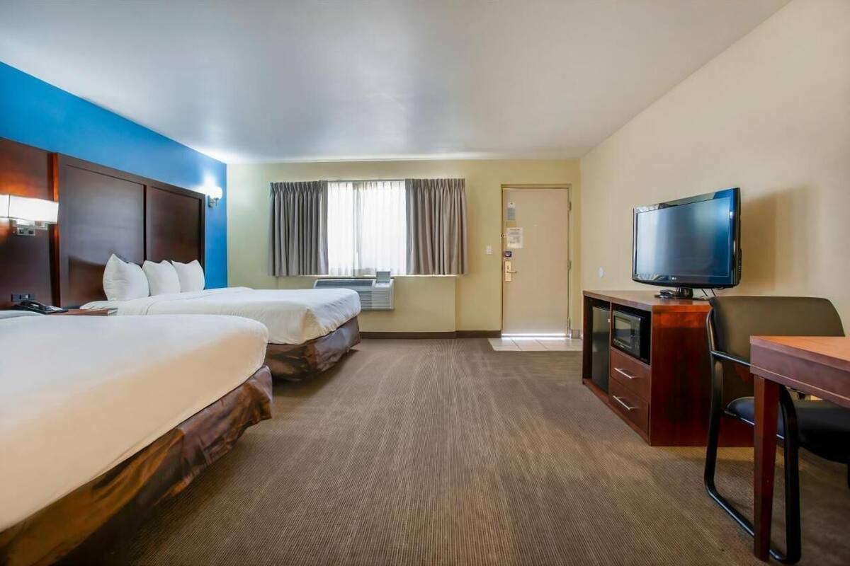 A hotel room with two beds, a desk with a TV, and a window with curtains.