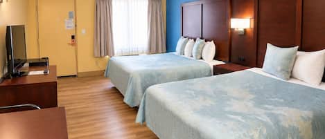 Habitación de hotel con dos camas, un escritorio, televisor y ventana con cortinas.