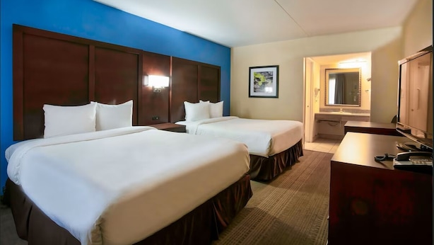A hotel room with two beds, a desk, a mirror, and a framed picture on the wall.