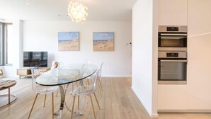 Une cuisine moderne dotée d’appareils électroménagers en acier inoxydable, une table à manger en verre avec des chaises transparentes et des œuvres d’art accrochées aux murs.