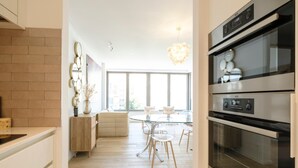 Une cuisine moderne dotée d’appareils électroménagers en acier inoxydable, un coin repas avec une table et des chaises en verre, et un mur décoratif en briques.