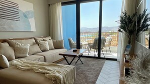 Una sala de estar moderna con un sofá, una mesa de centro y vistas a una piscina y montañas a través de grandes ventanales.