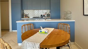 Una cocina moderna con armarios azules, encimera blanca y un comedor con mesa de madera y sillas acolchadas.