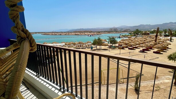 Un balcón con vista a la playa, una silla de descanso y una zona de piscina.
