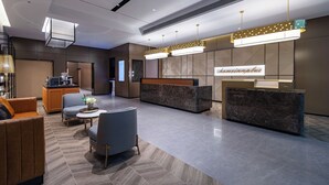 A modern hotel lobby with a reception desk, seating area, and a kitchen in the background. - HomeInn Plus Guozhan Liufang Subway Stn (Beijing)
