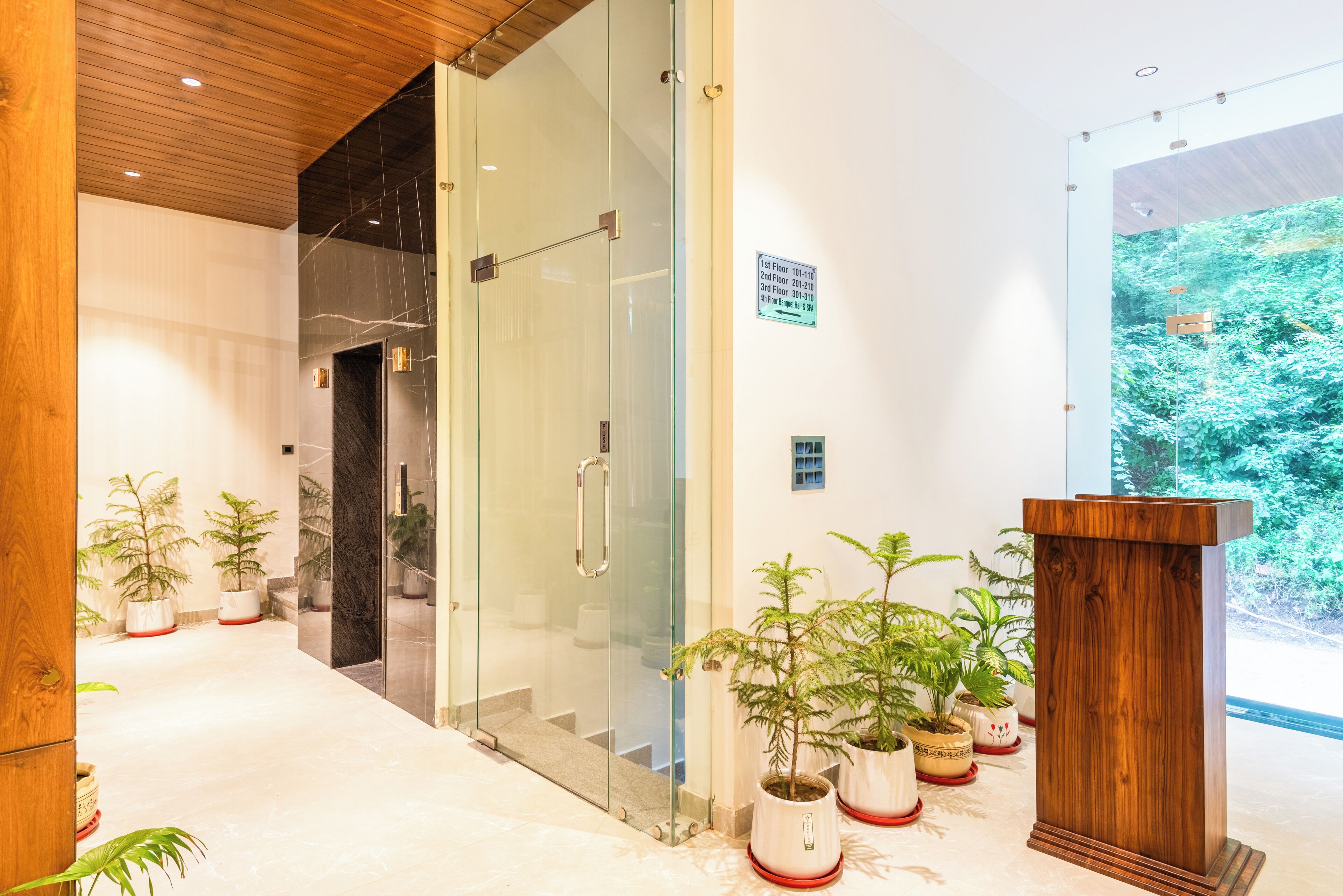 A modern lobby with glass doors, potted plants, and a wooden podium.