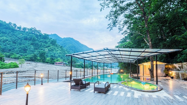 A swimming pool area with a glass enclosure, lounge chairs, and a lamp post. - DLS Divine River Resort and Spa (Rishikesh)