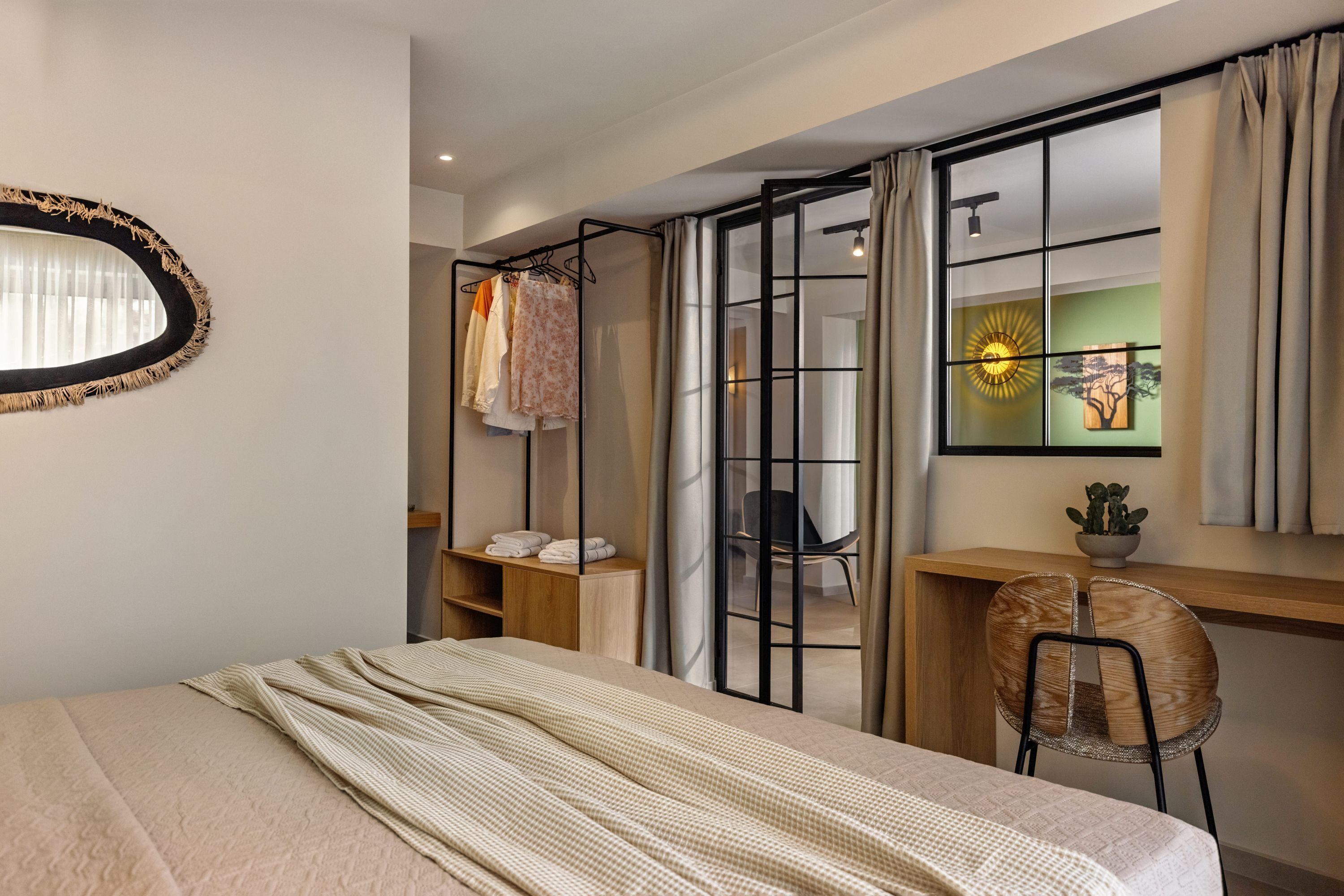 A bedroom with a bed, a wooden desk, a chair, a hanging clothes rack, and a window with curtains.