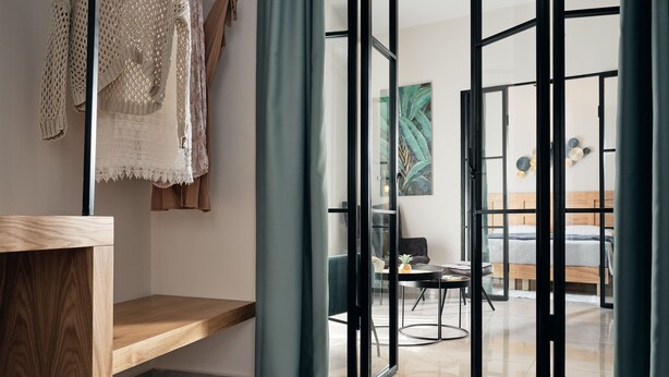 Et moderne hotelværelse med en træbænk, en glasdør, der fører til en balkon, og en seng med en trægavl.