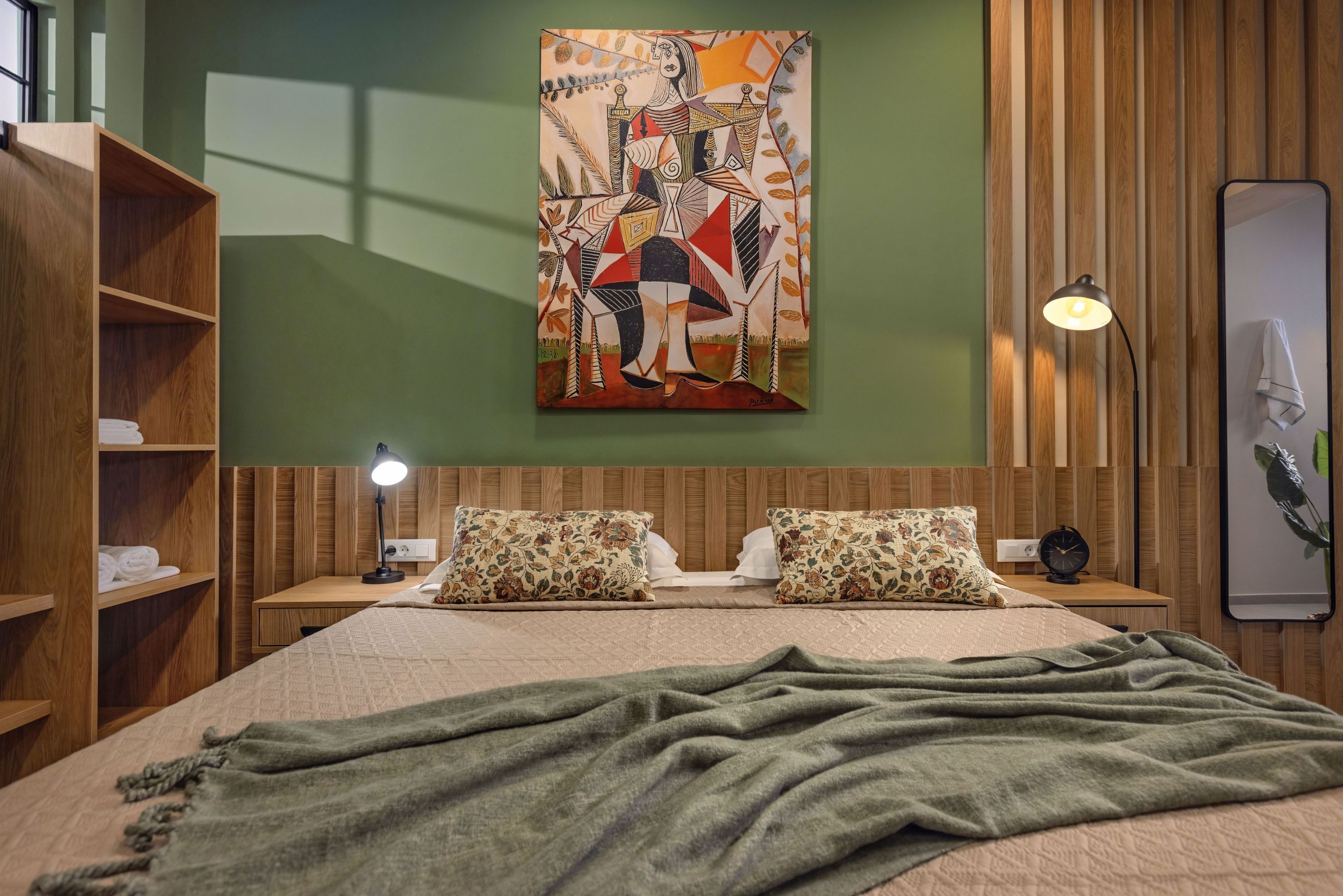 A modern bedroom with a bed, wooden headboard, a painting, a bedside lamp, and a nightstand.