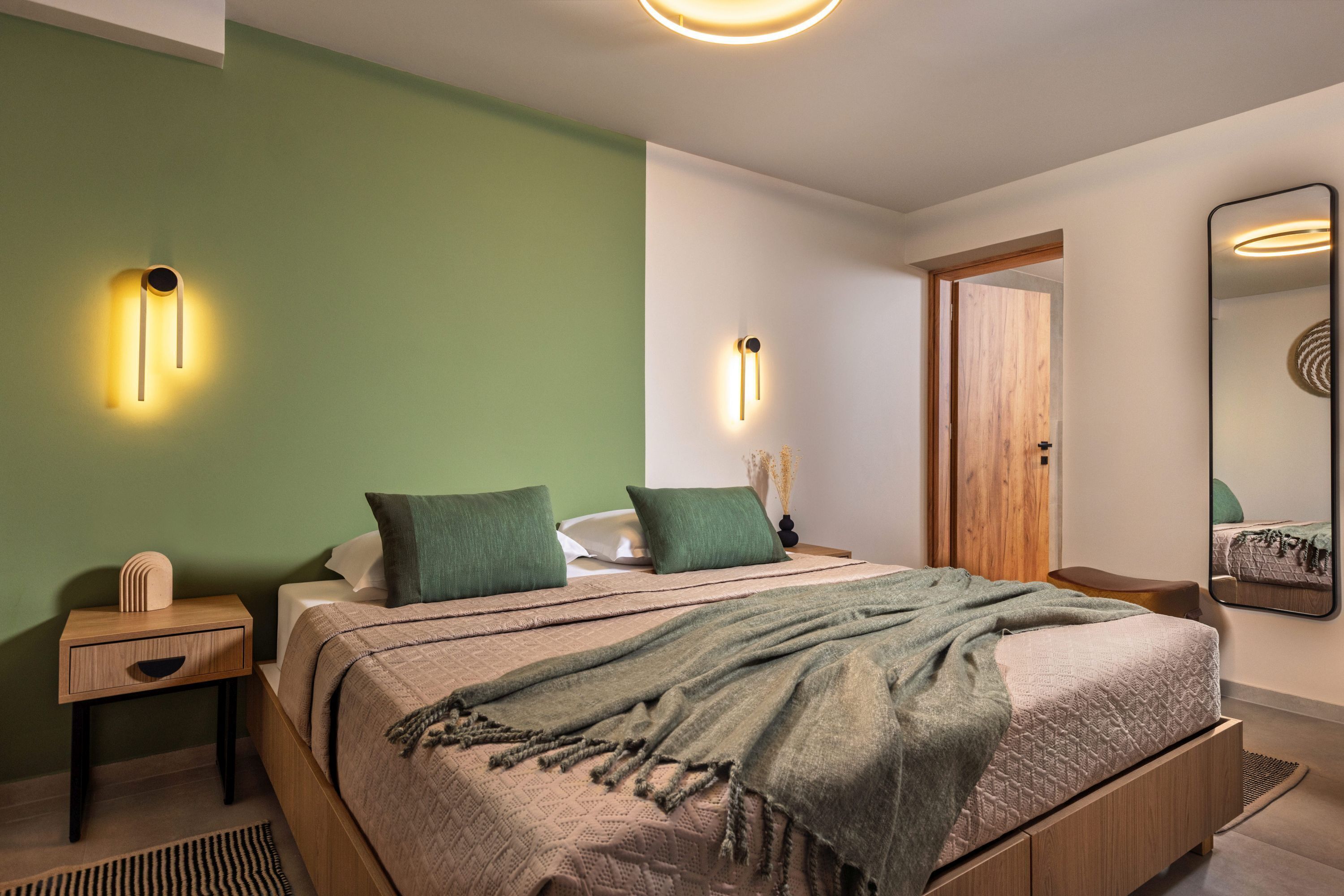 Une chambre à coucher moderne avec un lit, des tables de chevet, une commode, un miroir et une porte.