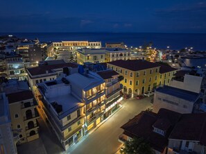 Un pueblo costero al anochecer con edificios iluminados, un puerto deportivo y una vista despejada del mar.