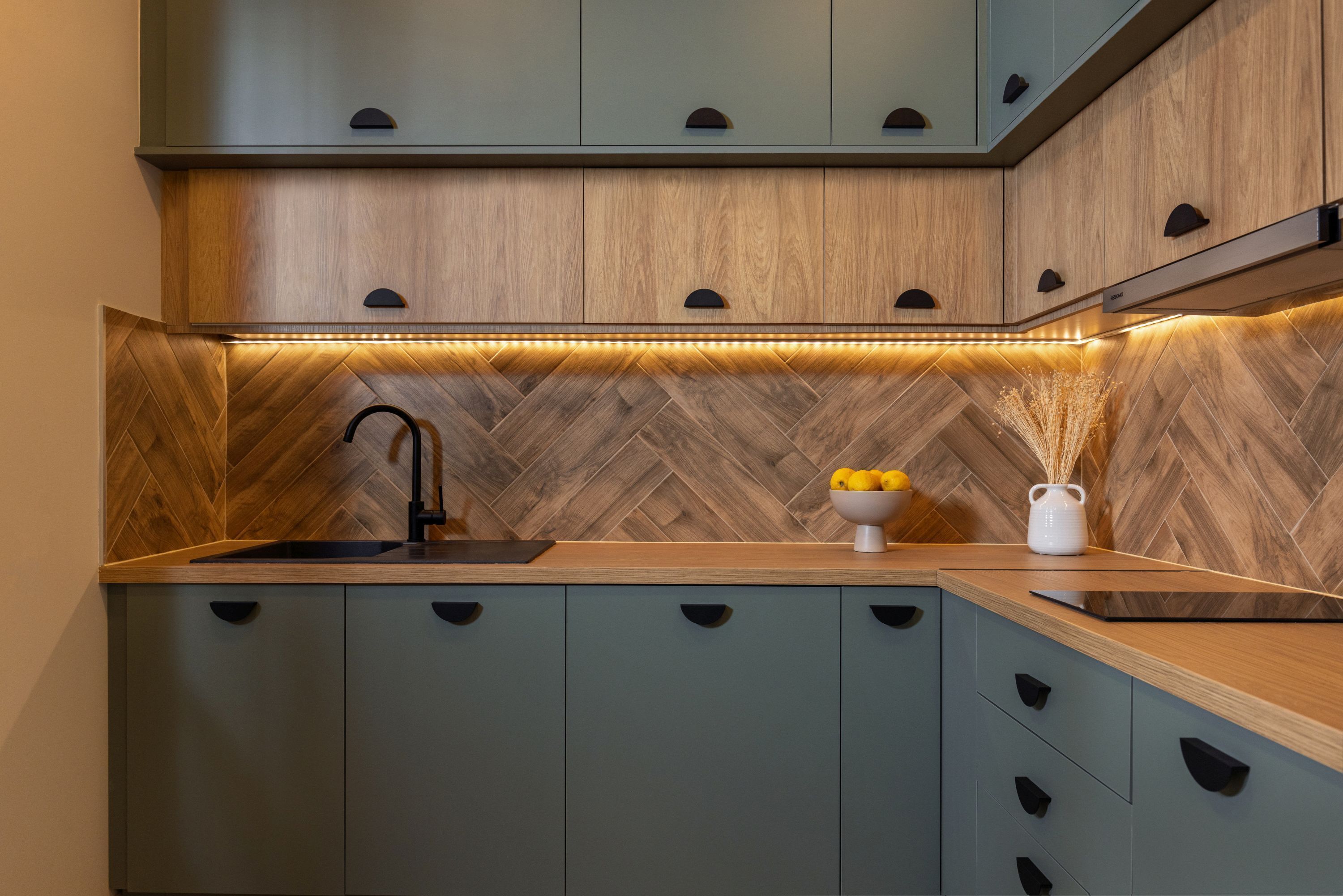 Cozinha moderna com armários de madeira, painel de backsplash em padrão herringbone e iluminação sob os armários.