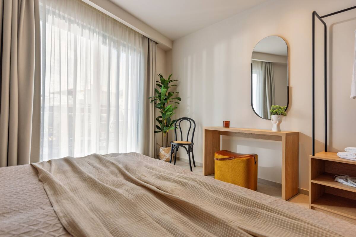 Une chambre d’hôtel avec un lit, un bureau, une chaise, un miroir et une plante.
