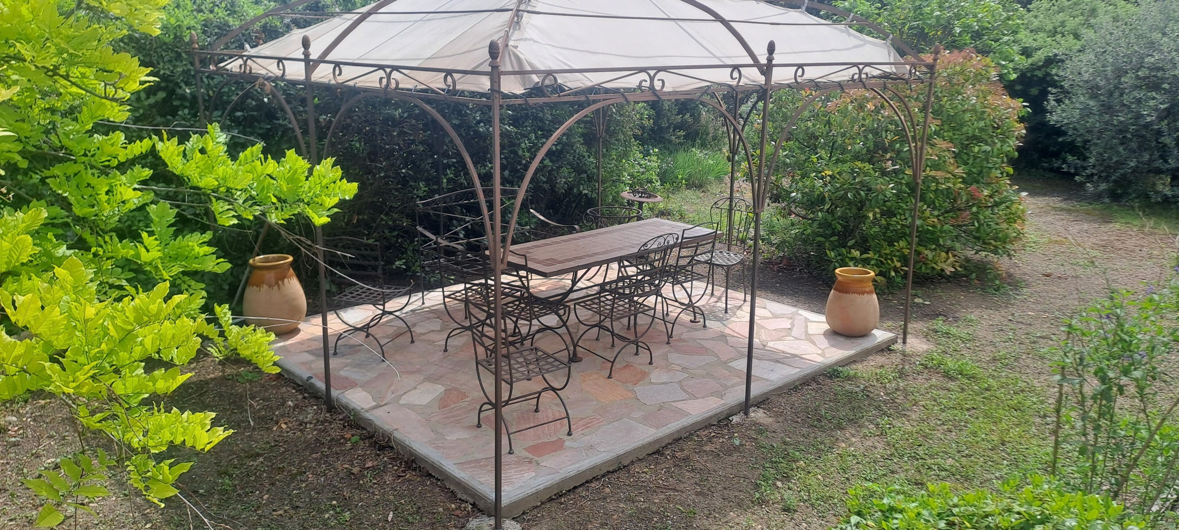 A gazebo with a table and chairs, surrounded by greenery.