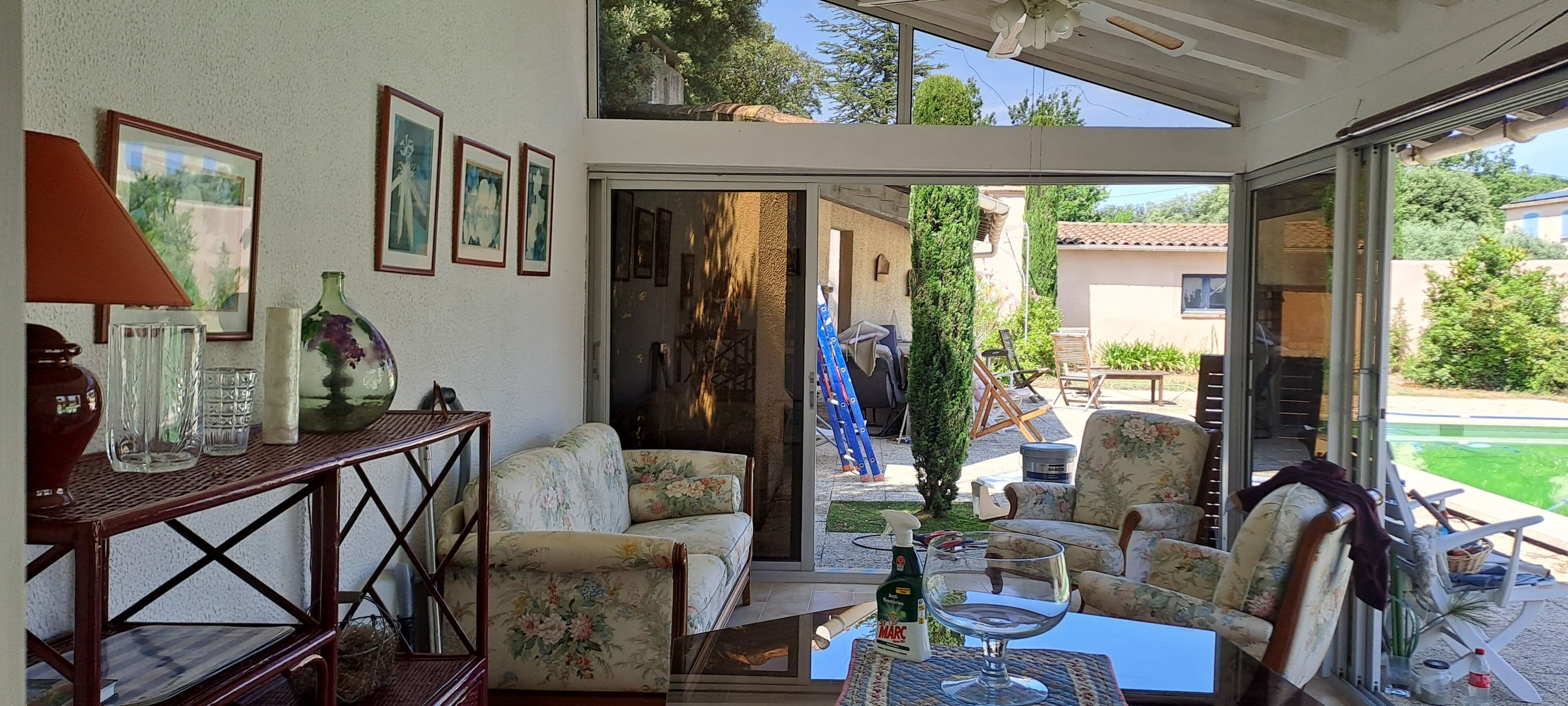 A sunlit patio with a sofa, chairs, a table, and a glass door leading to an outdoor area with a pool.