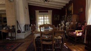 A dining room with a wooden table and chairs, a chandelier, and a view through a window with curtains. - House in Provence (Chateauneuf de gadagne)