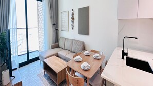 A modern living space with a sofa, dining table, chairs, and a kitchen area. - Premium Belvilla 1Bedroom in JVC with Pool & Gym (Dubai)