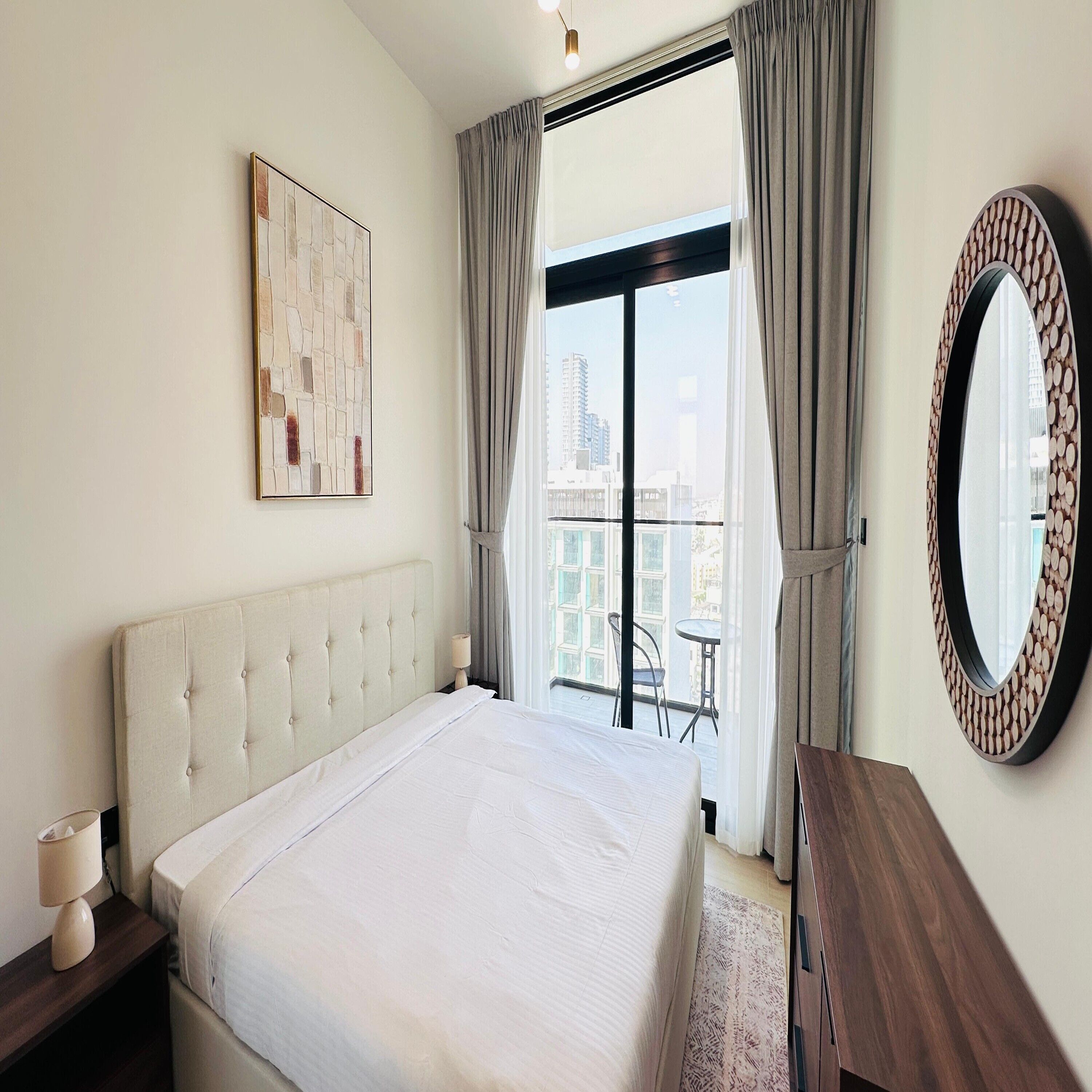 Een slaapkamer met een groot bed, een ronde spiegel, een schilderij en uitzicht op de stad.