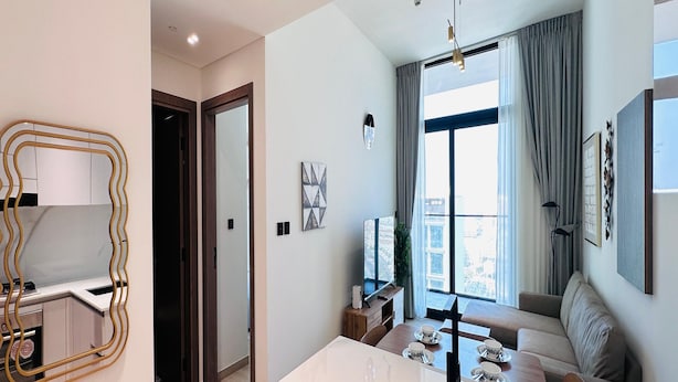 A modern kitchen with a marble countertop and a sink, a dining area with a table set for four, and a living area with a sofa and a large window. - Premium Belvilla 1Bedroom in JVC with Pool & Gym (Dubai)